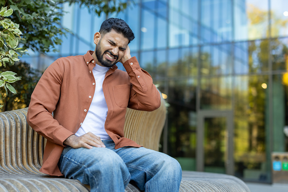 Young man with sore ear sits on park bench.